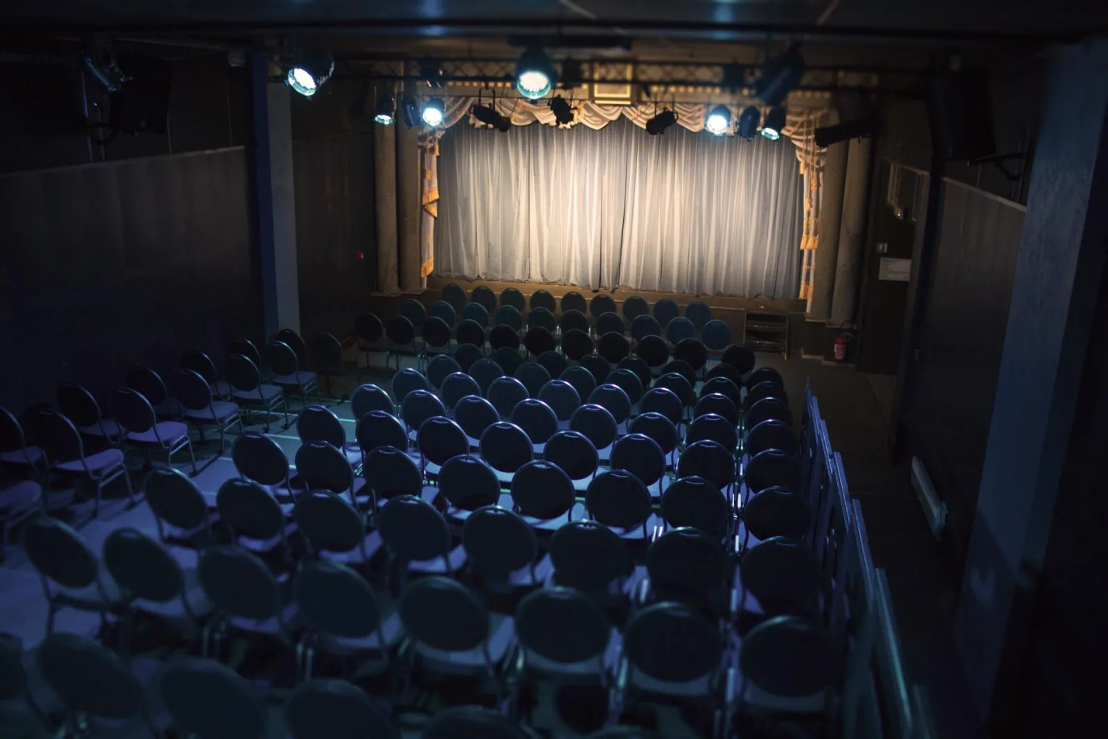 Vue intérieure du Théâtre Victoire de Bordeaux montrant les rangées de sièges vides face à la scène illuminée avec rideau blanc et décors dorés