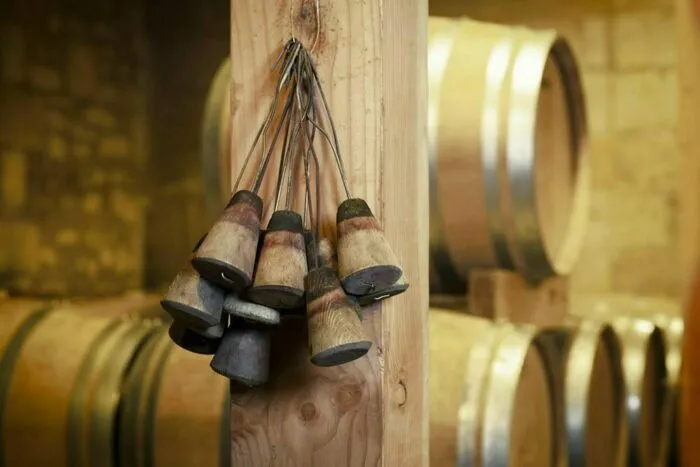 Clochettes de vendangeur suspendues à une poutre en bois dans une cave avec tonneaux de vin en arrière-plan, lors des Portes ouvertes aux châteaux de Castillon Côtes de Bordeaux