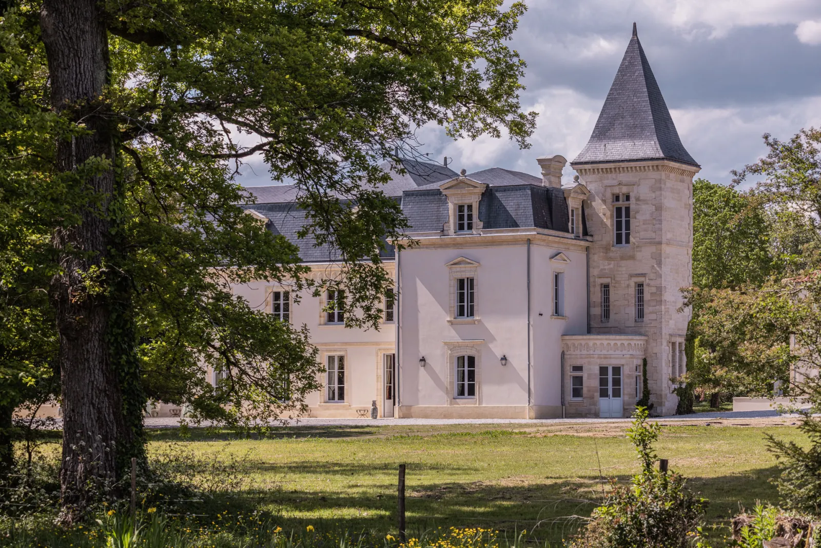 Château Sénéjac, demeure de style château fort avec tourelle pointue, façade rose pâle et toiture ardoisée, entouré de verdure et d'arbres centenaires dans la région de Bordeaux