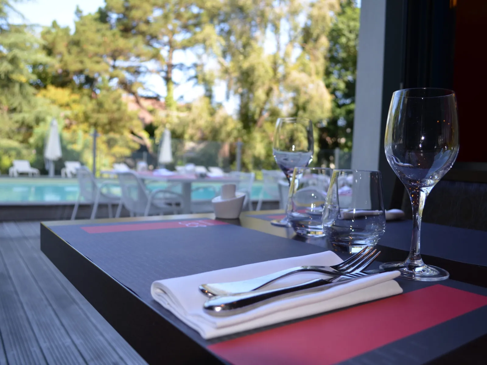 Table de restaurant élégante avec verres d'eau, couverts et serviette, vue sur piscine et arbres en arrière-plan à Bordeaux Côté Lac