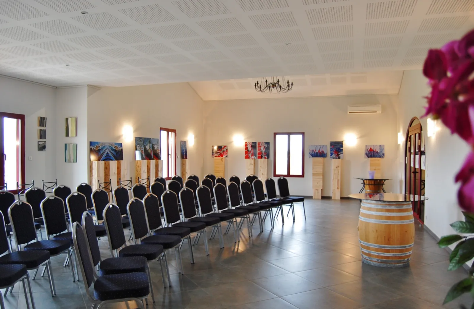 Salle de réception du Château Pichon Bellevue à Bordeaux avec des chaises noires alignées, un tonneau de vin décoratif, des photographies murales et un lustre, prête pour un événement.