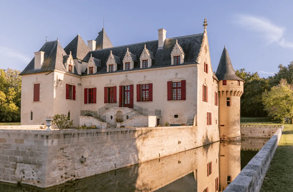 Château Olivier, forteresse médiévale avec façade blanche et toits d'ardoise, entourée d'un fossé rempli d'eau, près de Bordeaux