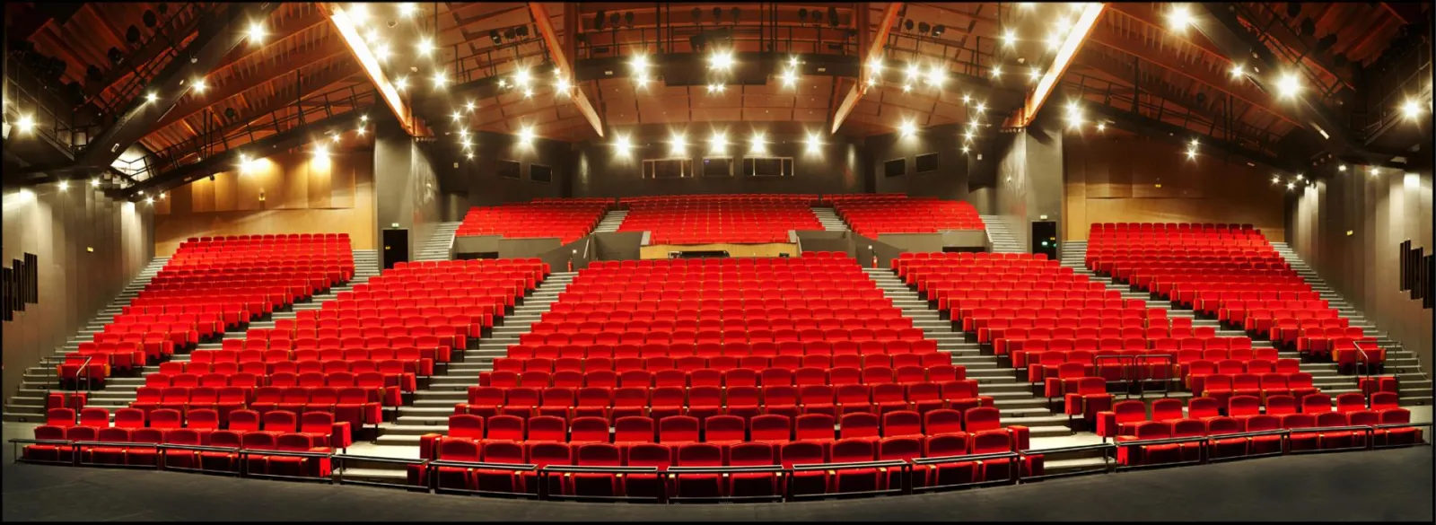 Salle de cinéma moderne avec des centaines de sièges rouges disposés en rangées, éclairage ambiant chaud et plafond en bois au Pin Galant à Bordeaux