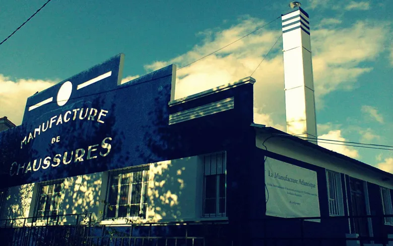 Façade de La Manufacture de Bordeaux, Centre de Développement Chorégraphique National, avec enseigne vintage bleue et cheminée blanche sous un ciel nuageux