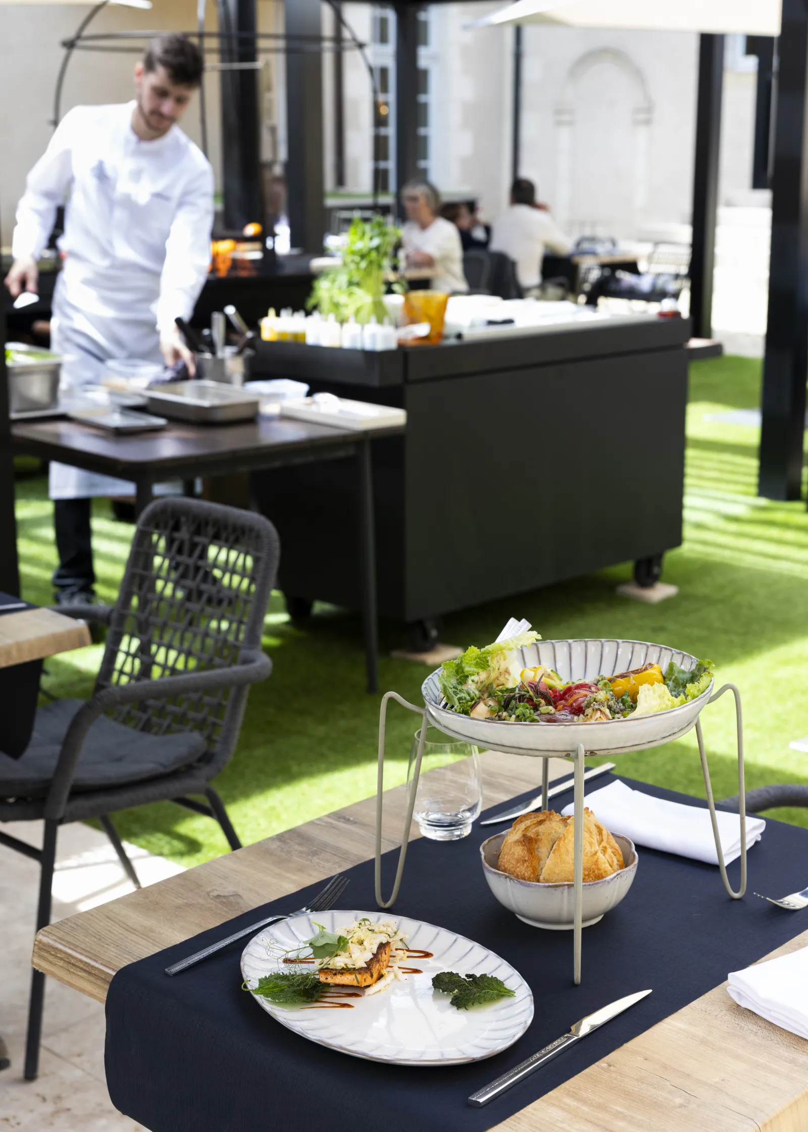 Terrasse de restaurant avec tables dressées, plats gastronomiques et personnel en cuisine, sur fond de gazon synthétique à Bordeaux