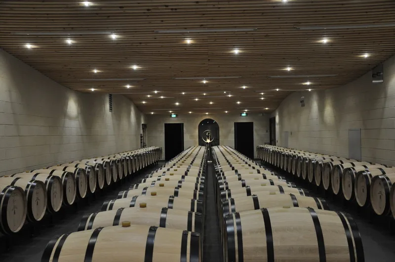 Rangées symétriques de fûts de chêne dans une cave de vinification moderne du Château Balestard La Tonnelle à Bordeaux, perspective centrale avec éclairage LED