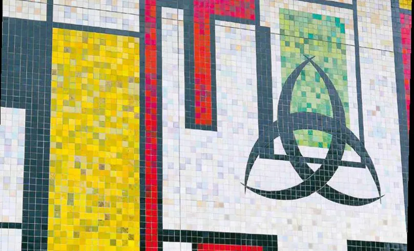 Mosaïque murale colorée de la Salle des Fêtes du Grand Parc à Bordeaux, composée de carreaux multicolores formant des motifs géométriques avec un symbole triangulaire vert et noir sur fond blanc, des bandes jaunes et rouges.