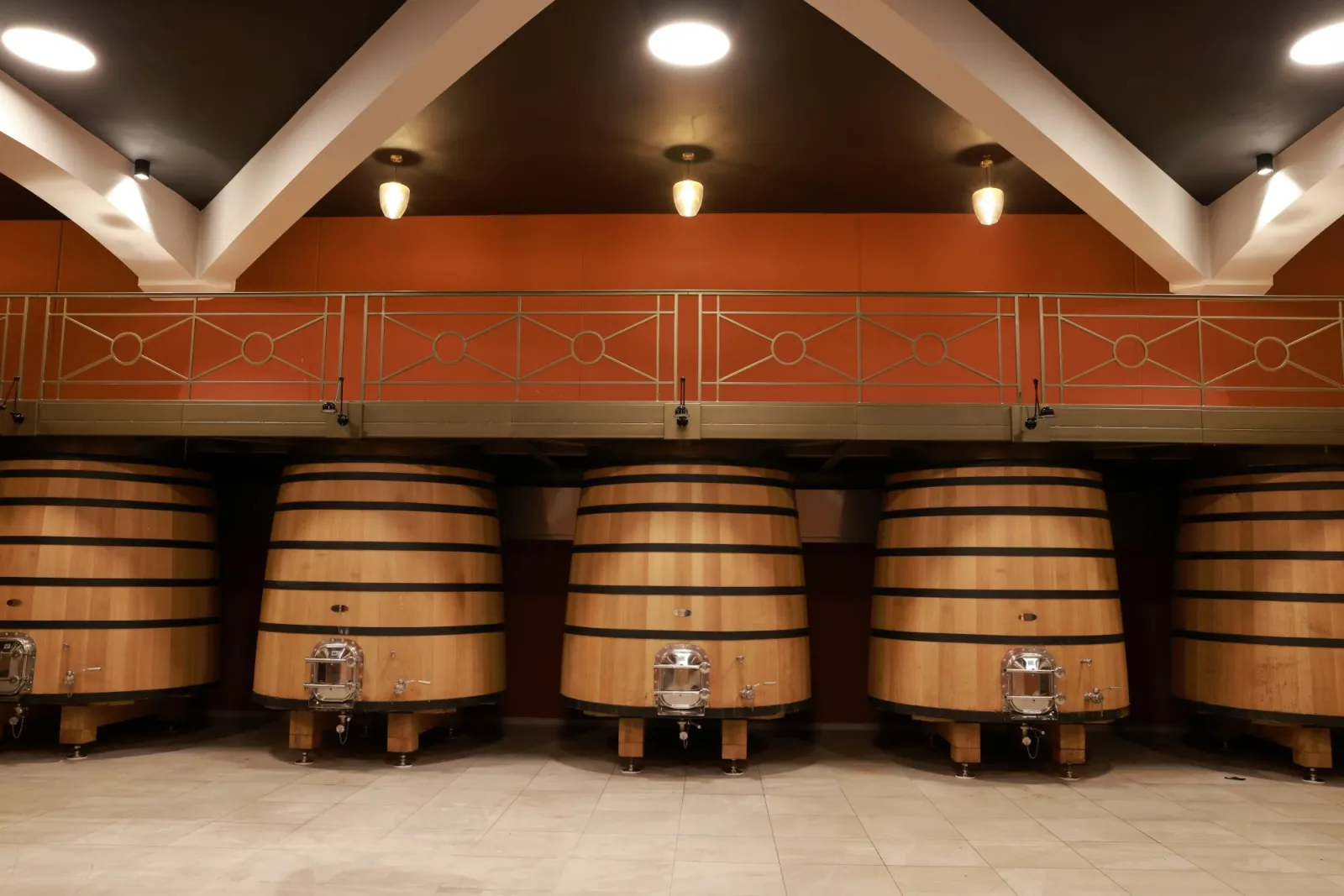 Chai de vinification avec cinq grands fûts en bois de chêne alignés sous un plafond cathédrale aux poutres blanches et murs orange, éclairage moderne, Château Plain Point à Bordeaux