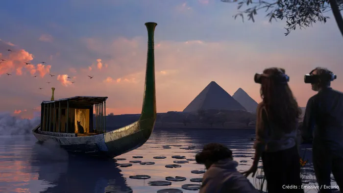 Vue immersive montrant une barque égyptienne stylisée avec voile verte naviguant devant des pyramides au coucher du soleil, avec des visiteurs observant la scène depuis le rivage.