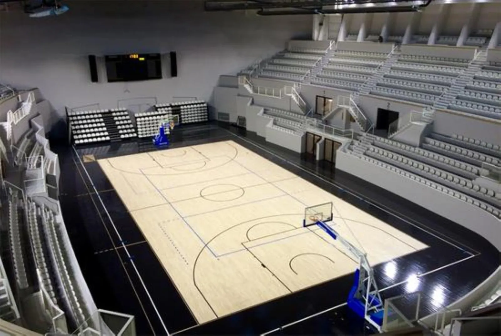 Vue aérienne du Palais des Sports de Bordeaux montrant un terrain de basketball avec gradins vides et deux paniers de basket bleus, dans une arène moderne équipée de sièges et de installations de qualité professionnelle.