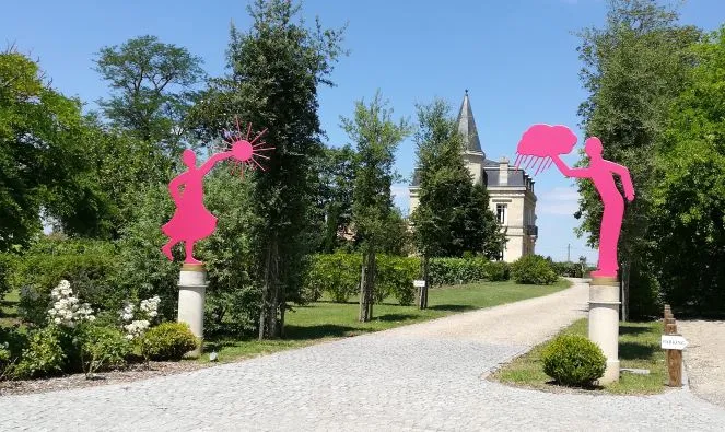 Allée d'accès au Château Yon-Figeac à Bordeaux avec sculptures roses abstraites de chaque côté, arbres verts et tour du château en arrière-plan