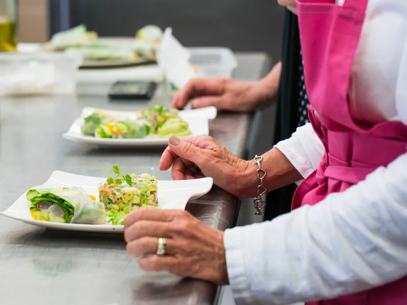 Deux femmes en tenue de chef participent à un atelier de cuisine au Château Kirwan à Bordeaux, préparant des plats avec salade et légumes sur des assiettes blanches.