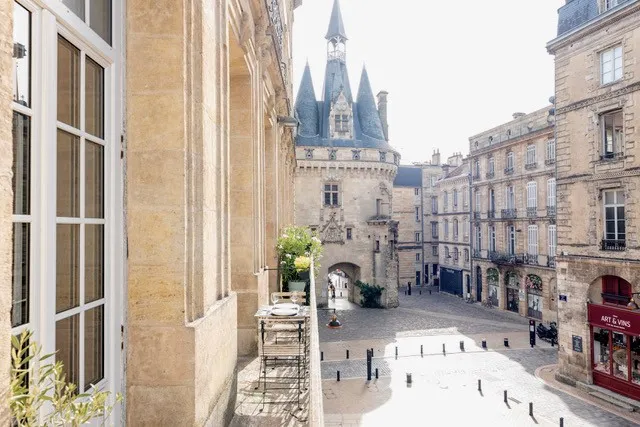 Vue panoramique de la Place de la Grosse Cloche à Bordeaux avec la tour médiévale du XIIIe siècle et ses toits pointus, entourée de bâtiments historiques en pierre blonde.