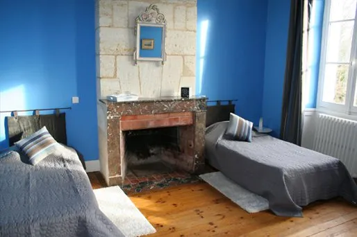 Chambre bleue du Château Valoux à Bordeaux avec deux lits jumeaux, une cheminée en marbre et un parquet en bois.