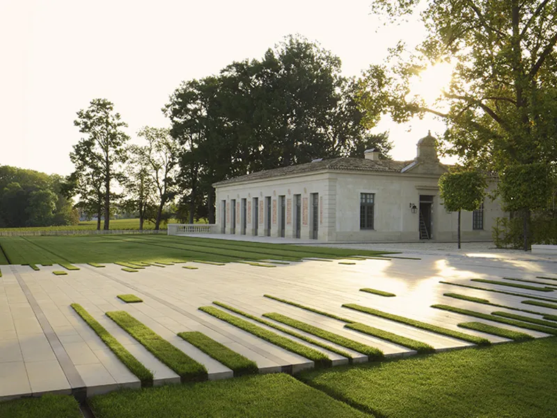Château Marquis d'Alesme Becker à Bordeaux, bâtiment blanc néoclassique avec colonnes, entouré d'un parc avec terrasse dalles et bandes d'herbe.