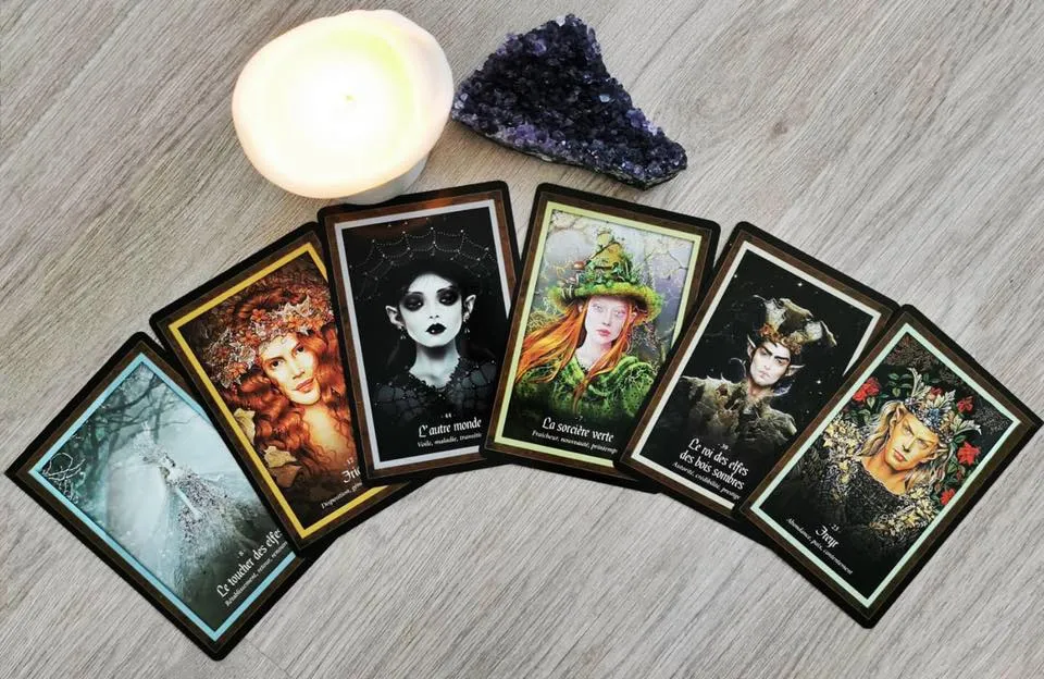 Arrangement de cartes de tarot avec inscriptions en français, une bougie blanche allumée et une pierre améthyste violette sur fond de bois gris.