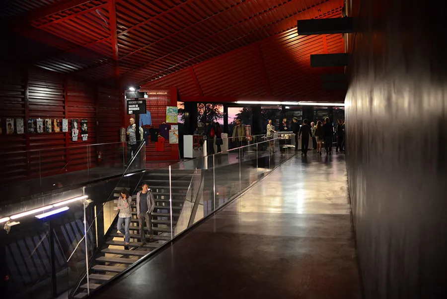 Intérieur du Rocher de Palmer à Cenon, Bordeaux : hall moderne aux murs rouges avec escaliers, passerelles métalliques et visiteurs circulant dans l'espace.