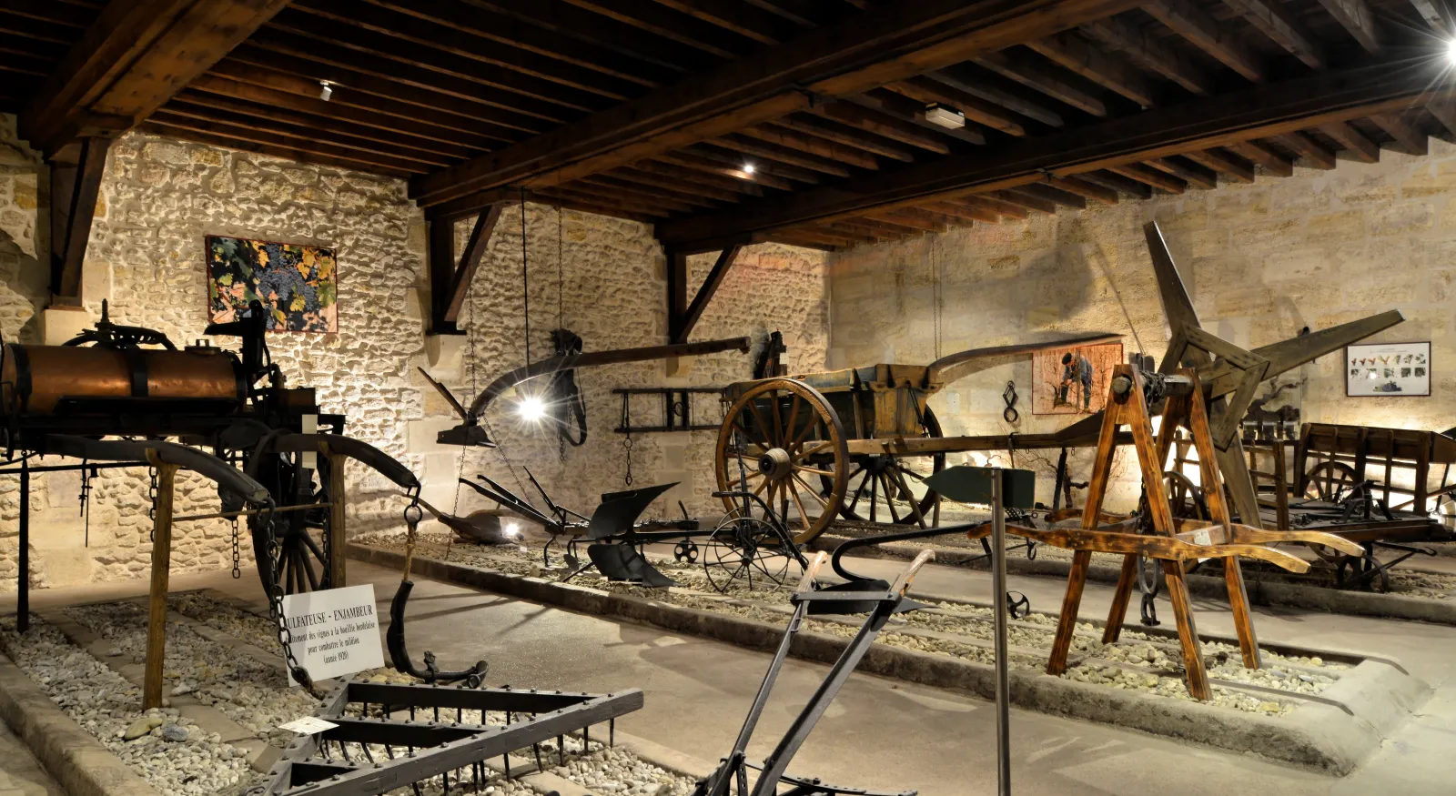 Intérieur du musée des Arts et Métiers de la Vigne et du Vin à Bordeaux présentant une collection d'outils et machines agricoles historiques utilisés pour la viticulture, exposés dans une cave voûtée en pierre.