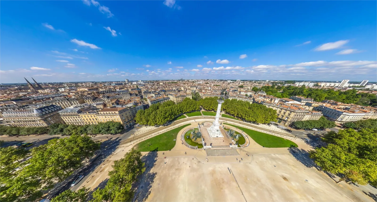 Luftaufnahme der Esplanade des Quinconces in Bordeaux, Frankreich, die den weiten Platz mit dem Girondins-Denkmal und den umliegenden Gebäuden unter klarem blauem Himmel zeigt.