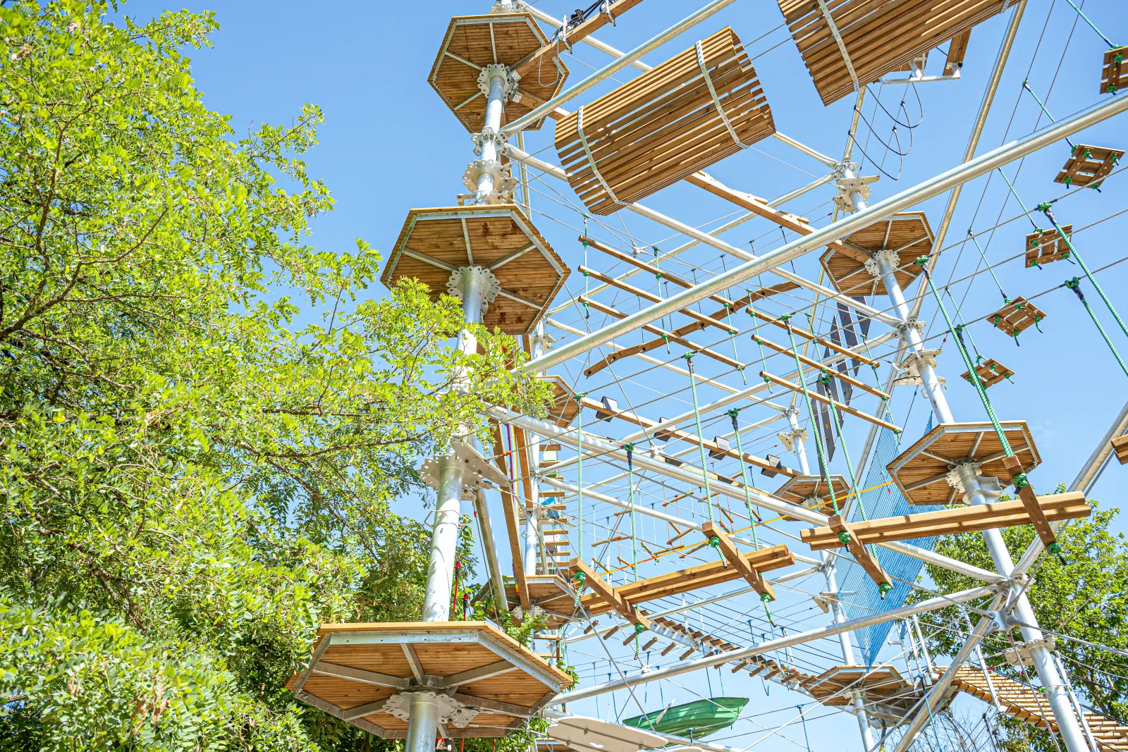 Les Cimes de Bordeaux Pessac, parc aventure en hauteur avec parcours de tyroliennes, ponts suspendus et filets de cordes entre les arbres sous un ciel bleu.