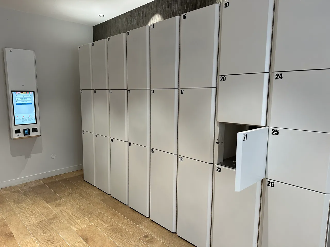 Rangée de casiers de stockage automatisés numérotés de 8 à 26 dans un Popin Locker à Bordeaux, avec un écran de commande tactile sur la gauche