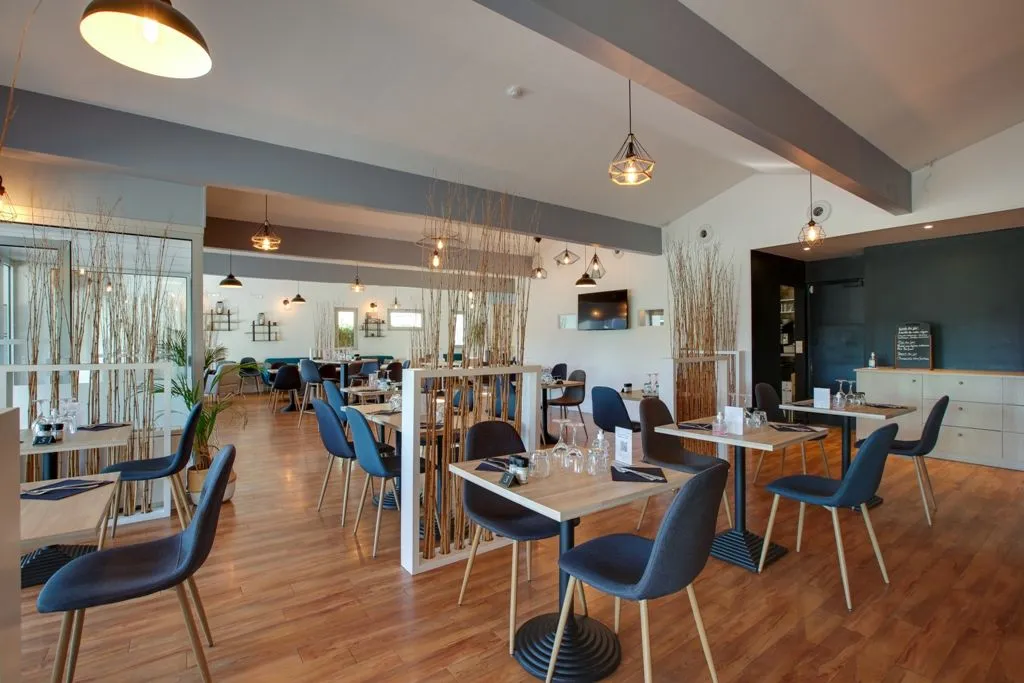 Intérieur moderne du restaurant Apolonia à Bordeaux avec tables en bois, chaises bleues, luminaires design, séparations en roseaux naturels et cuisine ouverte visible en arrière-plan