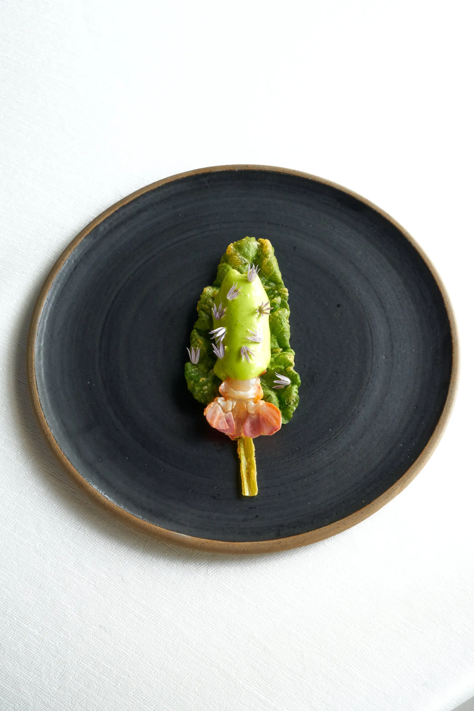 Assiette noire avec une création culinaire minimaliste composée de laitue verte, de saumon fumé et de microherbes, présentée de manière artistique au restaurant La Grand'Vigne à Bordeaux.