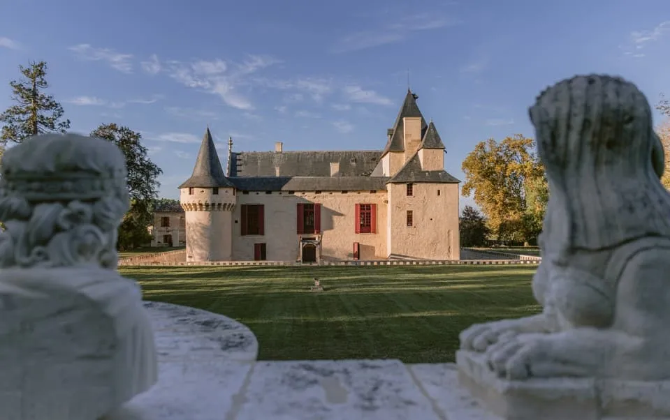 Le Château Olivier, un château médiéval avec tours et créneaux, entouré d'une pelouse verte et de statues de pierre en premier plan, situé près de Bordeaux.