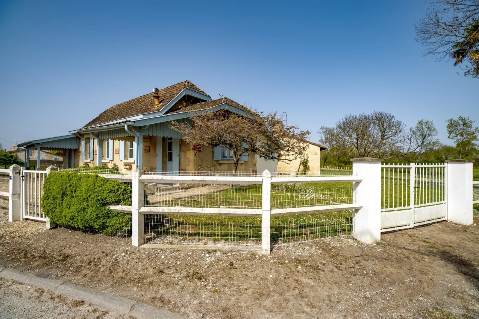 Maison bourgeoise de la Bastide de Siran à Bordeaux, avec façade jaune et bleu, entourée d'une clôture blanche, arbres en arrière-plan et ciel dégagé