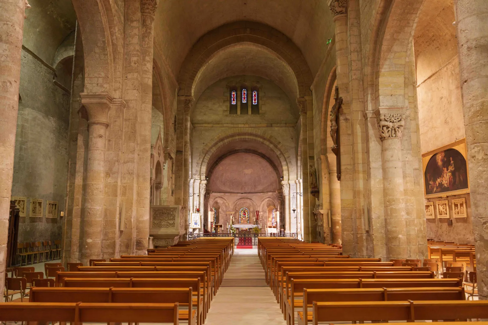 Intérieur de la basilique Notre-Dame-de-la-fin-des-Terres à Bordeaux, montrant la nef centrale avec ses colonnes en pierre, ses voûtes en berceau, ses bancs en bois et l'autel au fond illuminé par des vitraux.