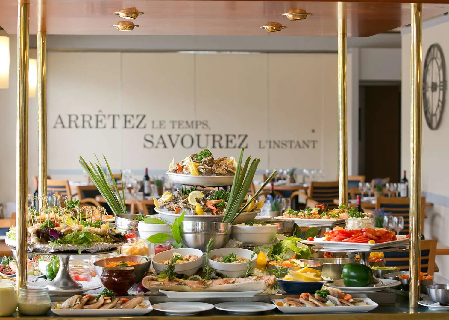 Buffet gastronomique avec assortiment de plats et fruits de mer dans un restaurant avec vue panoramique sur Bordeaux, orné d'une devise en français invitant à savourer l'instant