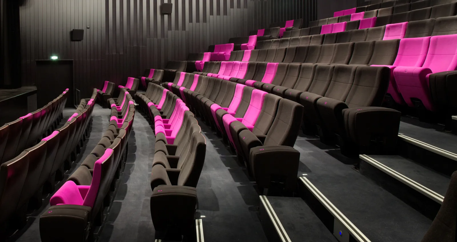 Intérieur d'une salle de cinéma moderne avec des fauteuils en cuir gris et des éléments luminescents rose vif, situé aux Colonnes à Blanquefort à Bordeaux.