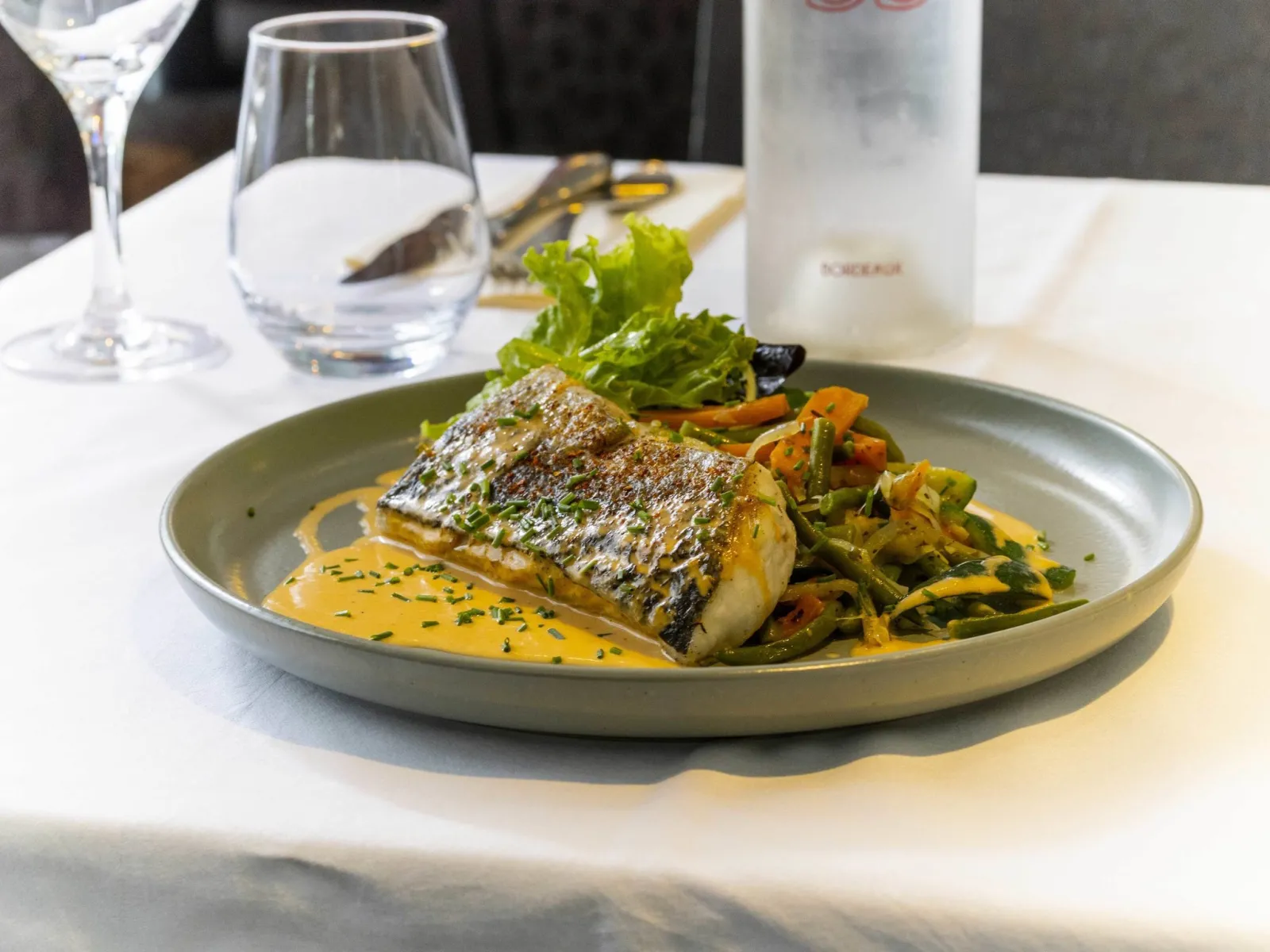 Filet de poisson grillé avec peau croustillante, servi sur une sauce dorée avec légumes sautés et salade verte, présenté dans un restaurant gastronomique à Bordeaux
