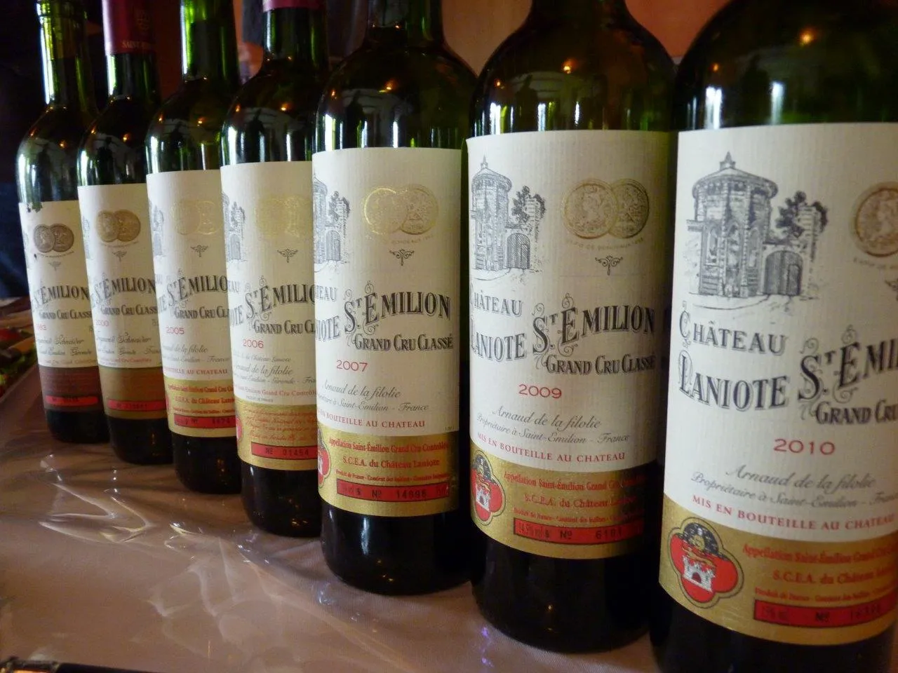 Collection de bouteilles de vin du Château Laniote, Grand Cru Classé de Bordeaux, millésimes 2007, 2009 et 2010, alignées sur une surface blanche.