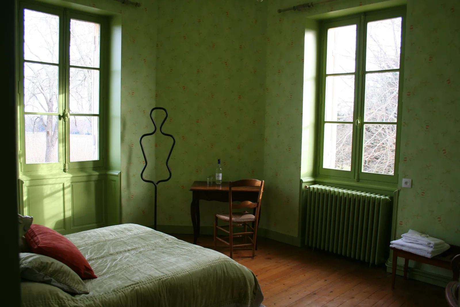 Chambre historique du Château Valoux à Bordeaux avec murs vert pâle, lit ancien, fenêtres à carreaux verts, mannequin de couture et mobilier d'époque