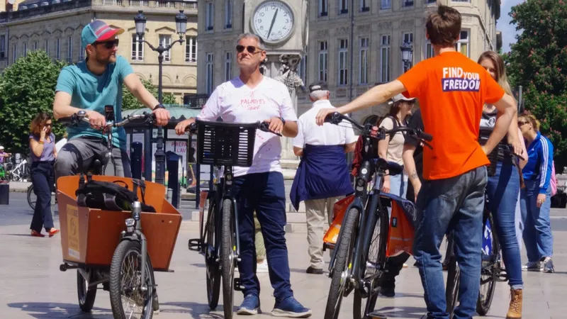 Groupe de cyclistes sur des vélos de location Holland Bikes, dont des vélos cargo orange, devant l'hôtel de ville de Bordeaux avec son horloge.