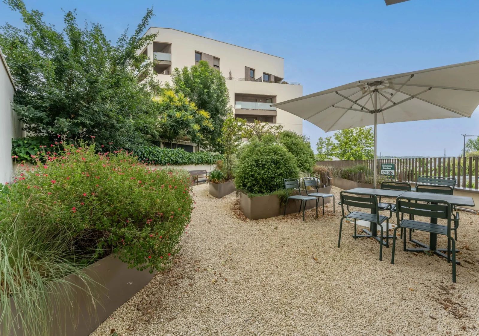 Terrasse extérieure de la résidence seniors Les Jardins d'Arcadie à Bordeaux avec tables, chaises, parasol, plantes en bacs et immeuble résidentiel en arrière-plan.