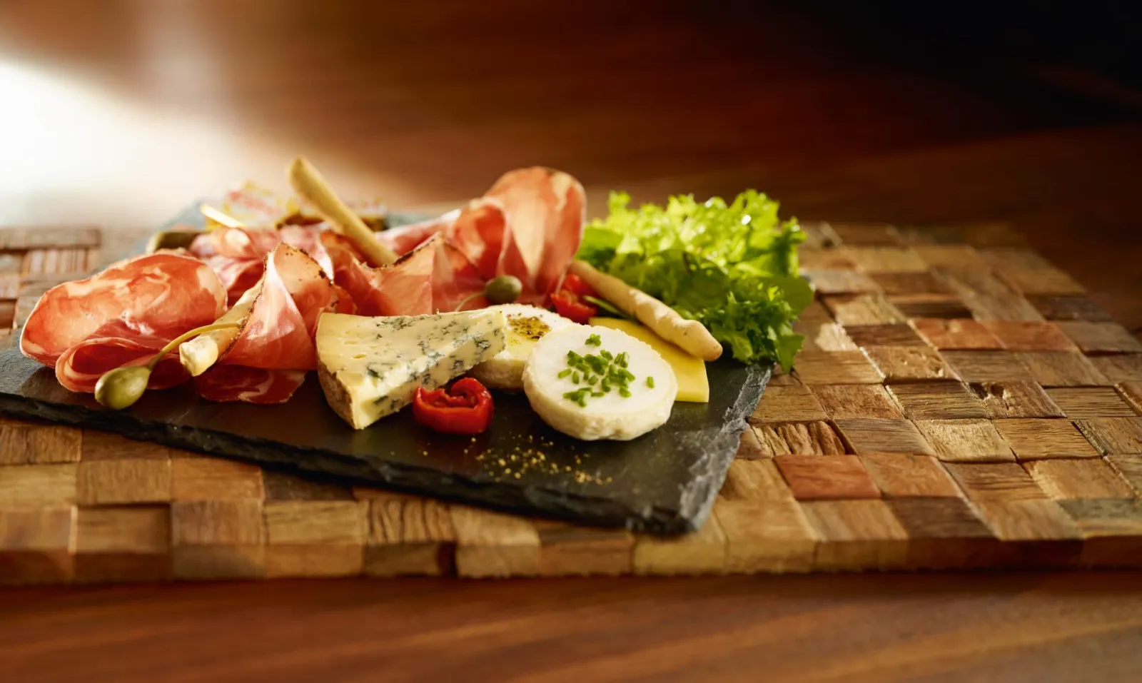 Plateau de charcuterie et fromages fins présenté sur ardoise avec prosciutto, fromage bleu, mozzarella, olives, cornichons, laitue fraîche et pain grillé