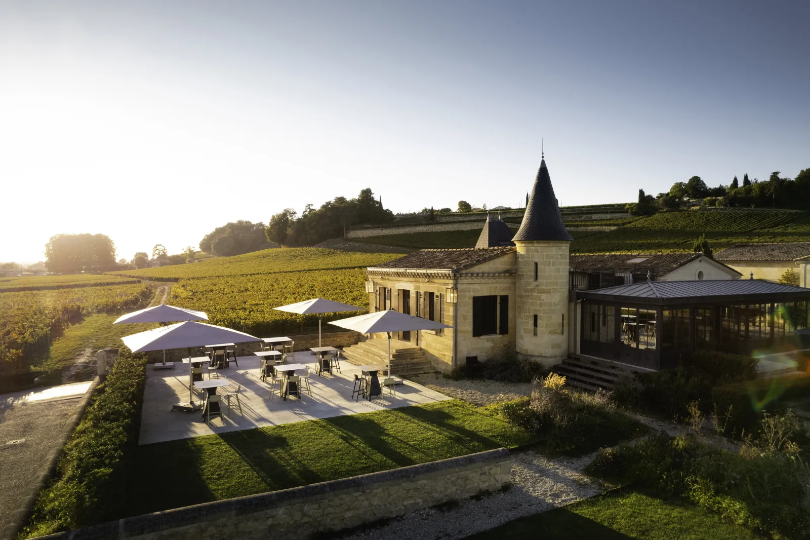 L'Atelier de Candale à Bordeaux : château avec tour pointue, terrasse ombragée et vignobles environnants au coucher de soleil