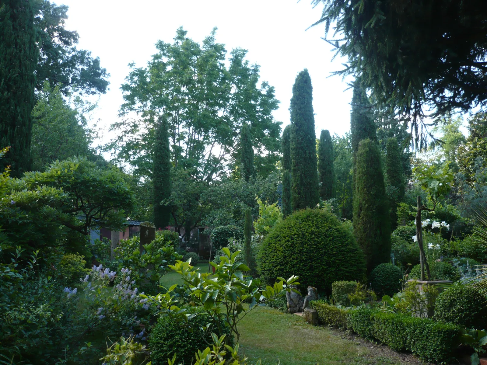 Vue du Jardin du Clozet à Bordeaux avec allée herbue, cyprès en colonnade, arbres feuillus, haies taillées et sculptures de pierre