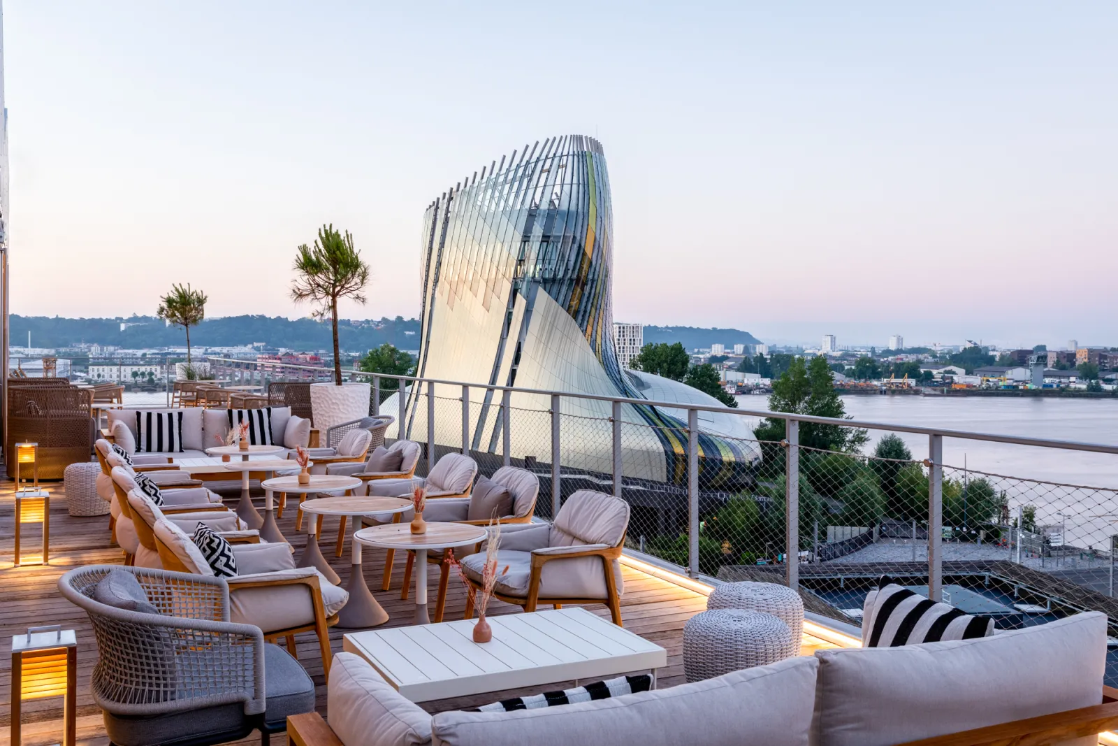 Terrasse panoramique à Bordeaux avec mobilier design, vue sur la Garonne et la Cité du Vin en arrière-plan au coucher du soleil