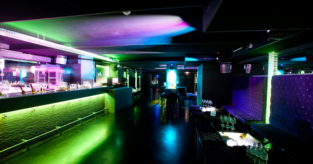 Intérieur du Boomboom Club à Bordeaux avec éclairage néon rose, vert et bleu, bar illuminé, sièges violets et ambiance de discothèque moderne