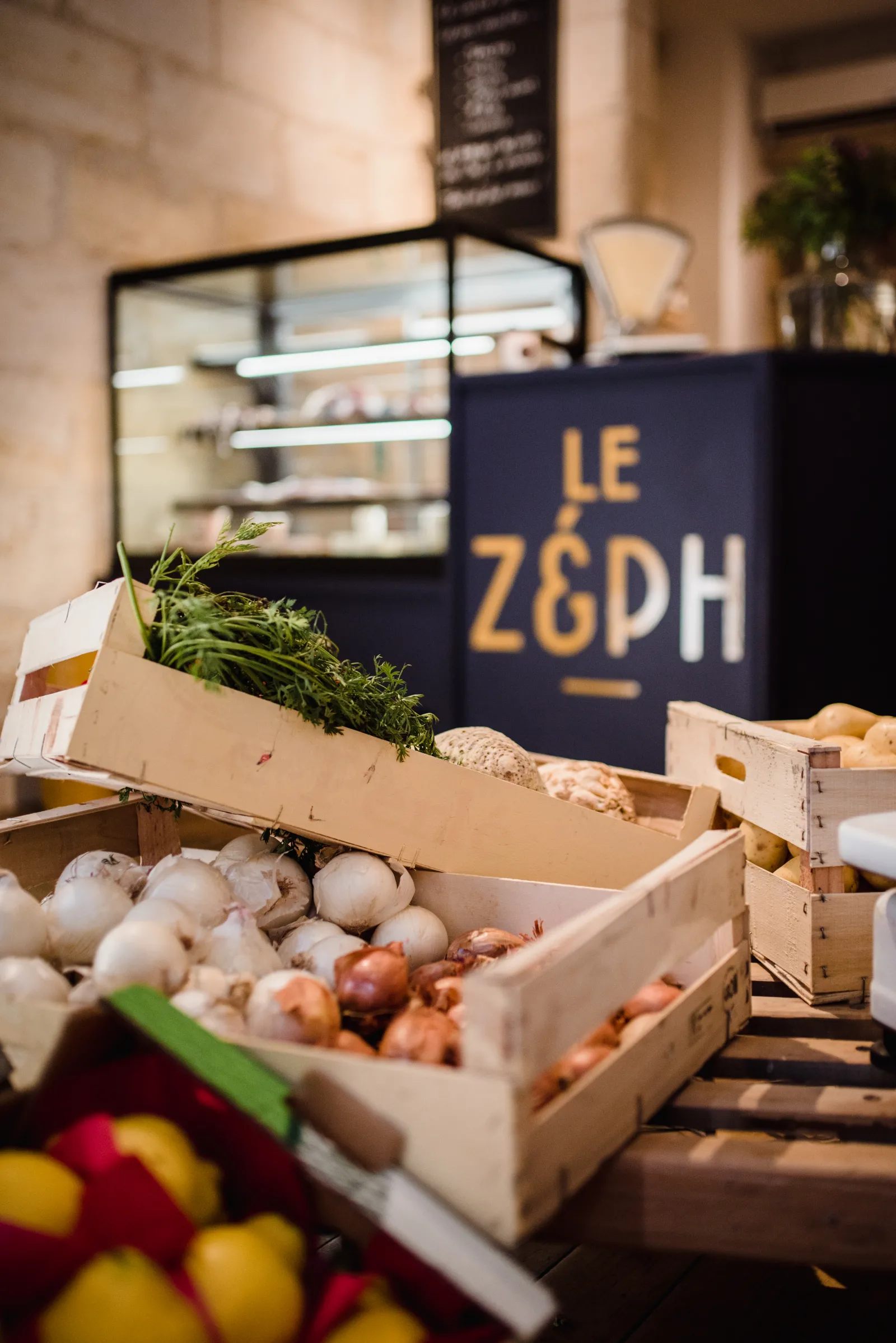 Étalage de fruits et légumes frais en caisses devant le restaurant Le Zeph' à Bordeaux, avec oignons, champignons, herbes et citrons visibles