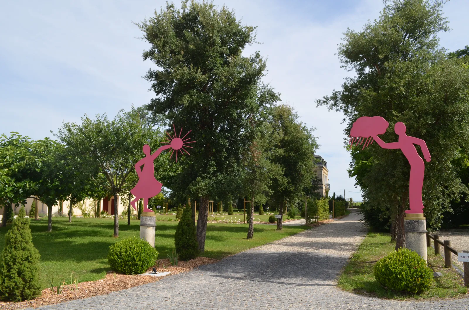 Allée bordée d'arbres avec deux sculptures roses représentant des figures humaines en silhouette, au Château Yon-Figeac à Bordeaux