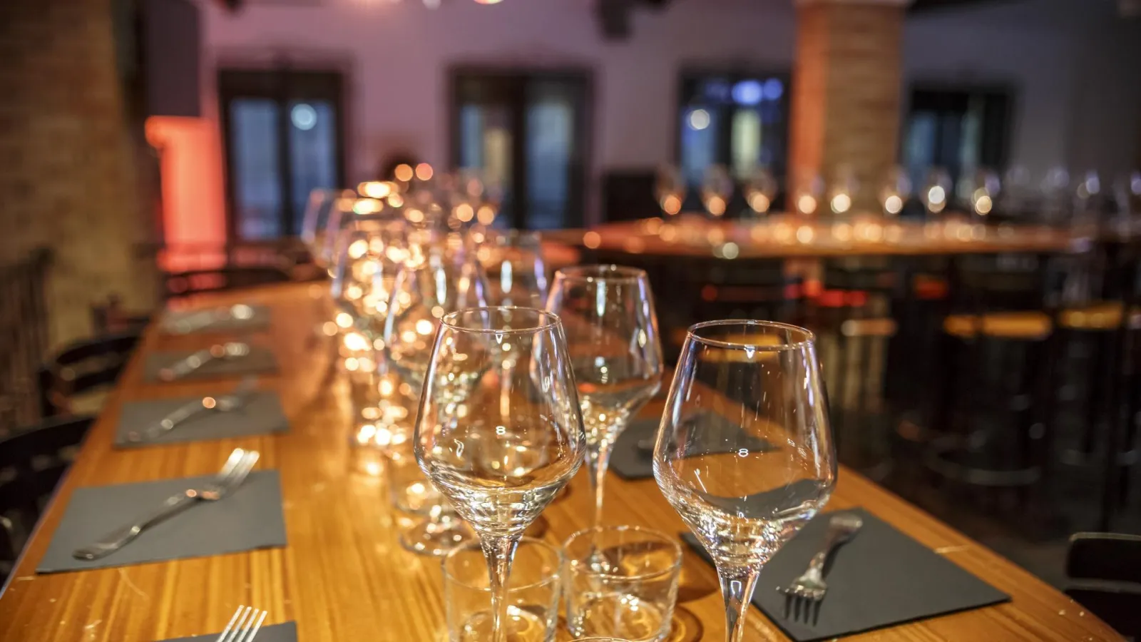 Table de dégustation à Bodega Bodega à Bordeaux avec verres à vin alignés, couverts et serviettes grises, éclairage chaleureux en arrière-plan