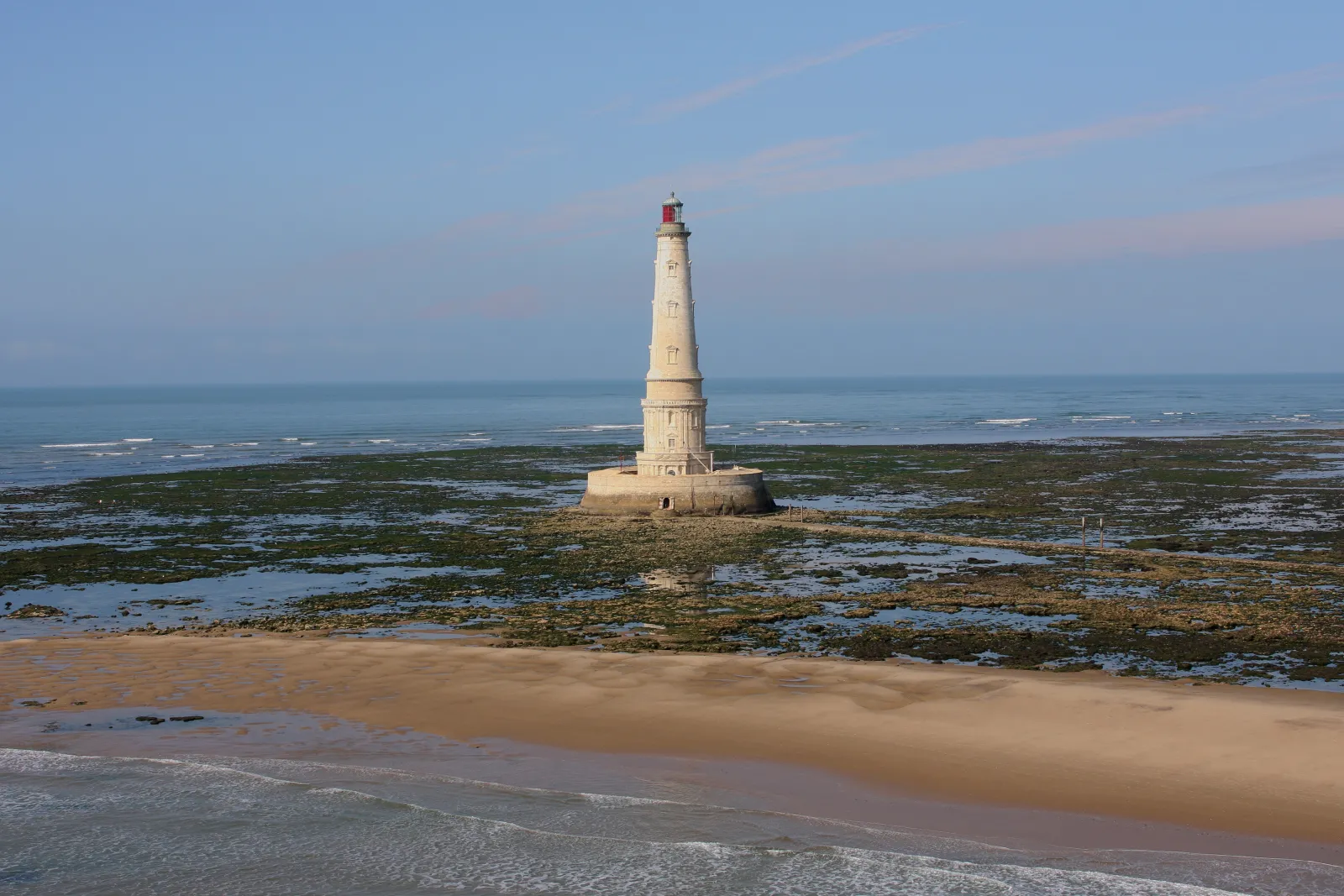 Le Phare de Cordouan, majestueux phare blanc sur un rocher en mer, accessible depuis la côte de Bordeaux à marée basse, entouré d'algues vertes et de sable.
