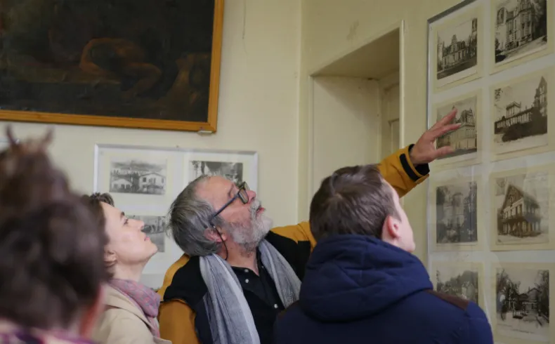 Un guide pointant des gravures historiques de bâtiments à des visiteurs dans une galerie du musée des Amis du Vieux Lormont à Bordeaux.