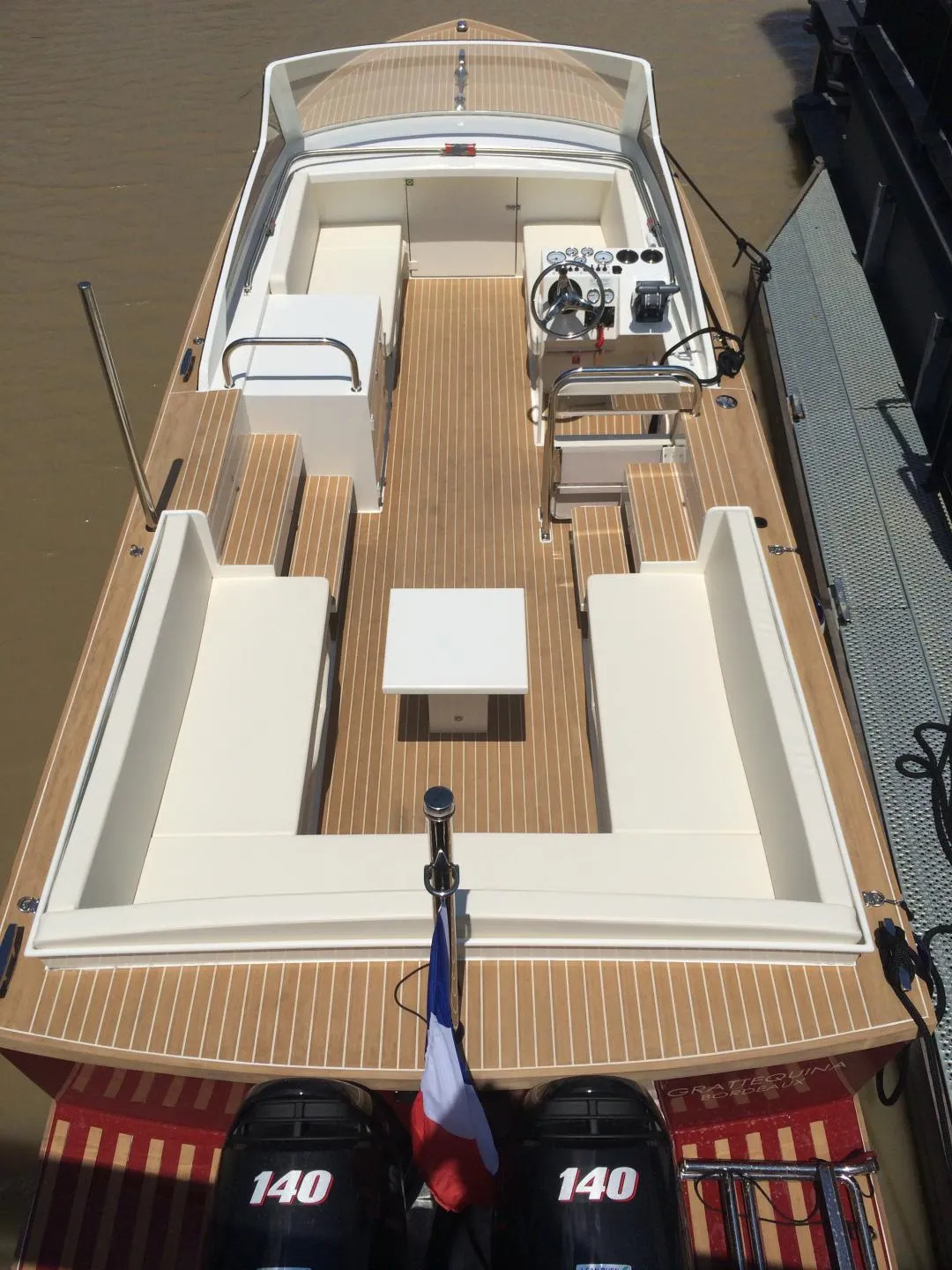 Vue aérienne du bateau taxi Grattequina à Bordeaux, montrant le pont en bois, la cabine de pilotage, les moteurs 140 chevaux et l'amarrage sur la Garonne