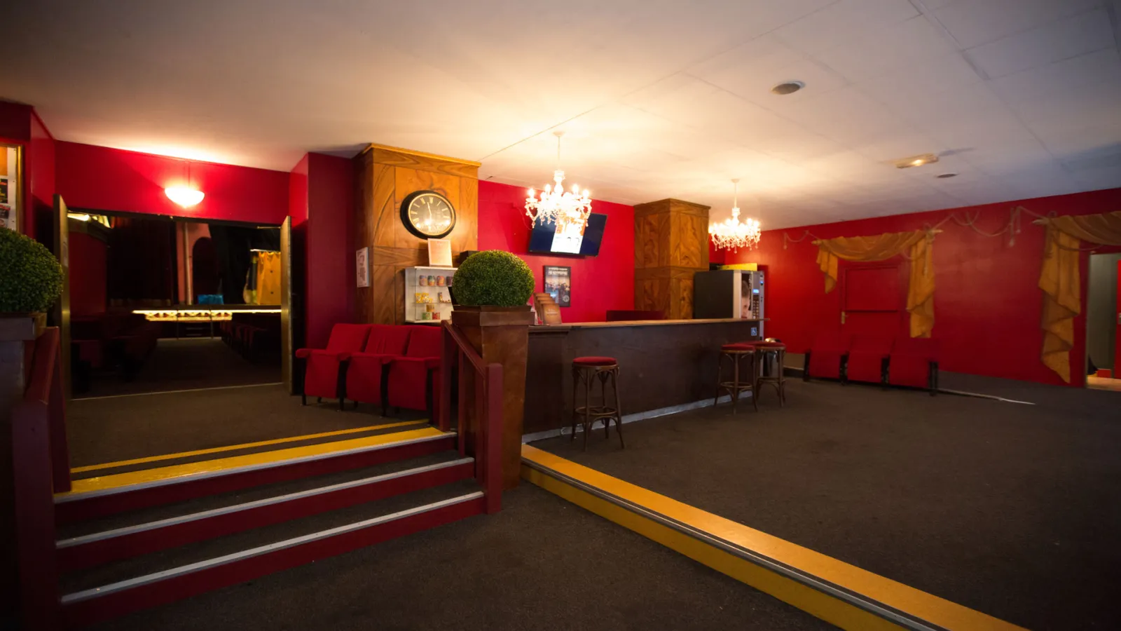 Lobby du Théâtre des Salinières à Bordeaux avec murs rouges, comptoir d'accueil en bois, sièges rouges, lustres et décoration élégante