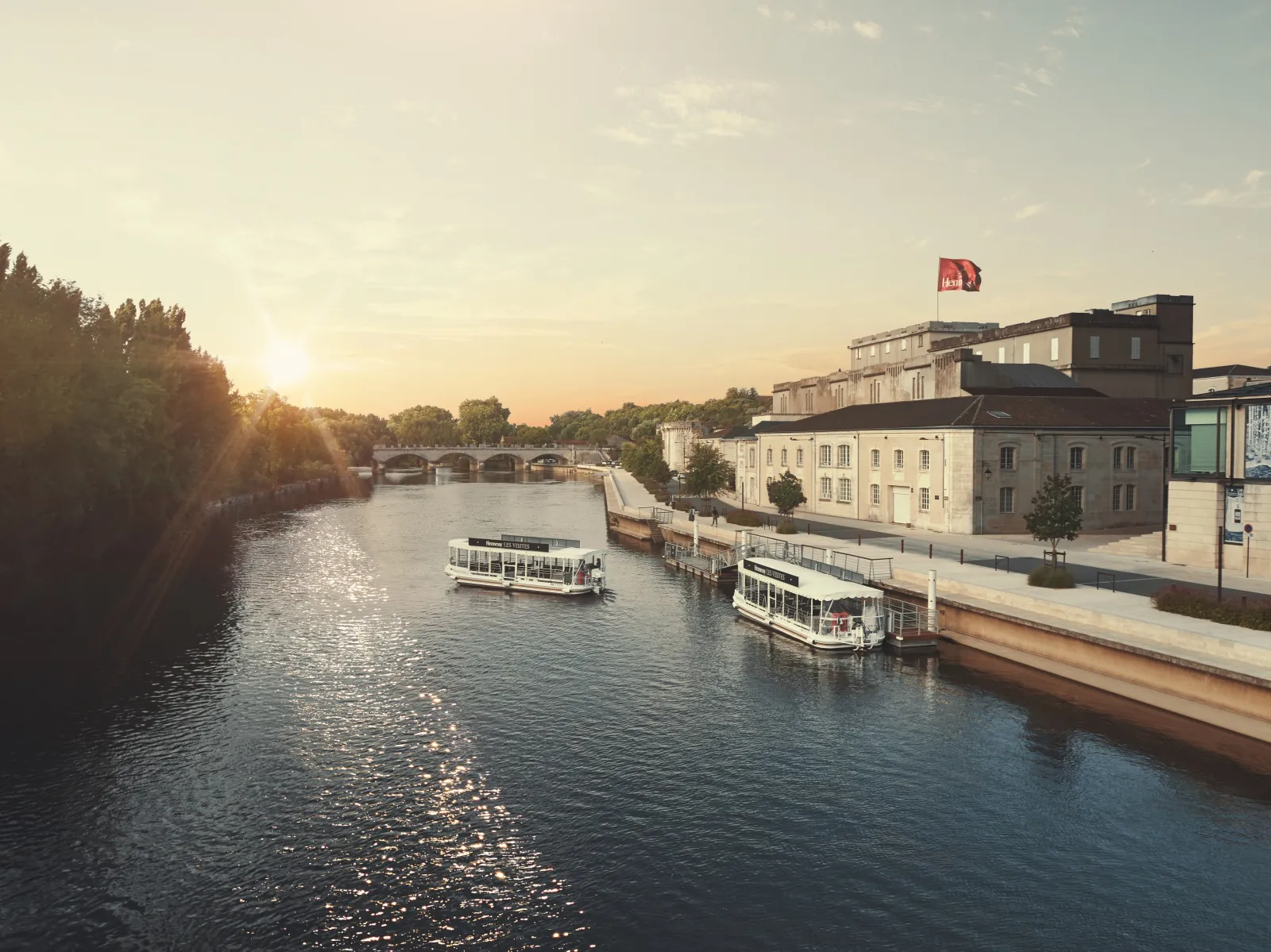 Vue panoramique de la Garonne à Bordeaux au coucher du soleil, avec des bateaux de croisière amarrés, des bâtiments historiques sur la rive droite et un pont en arrière-plan